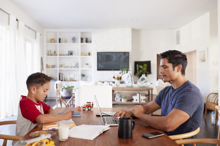 Hispanic father and son working opposite each other at the dining room table, side view, close up